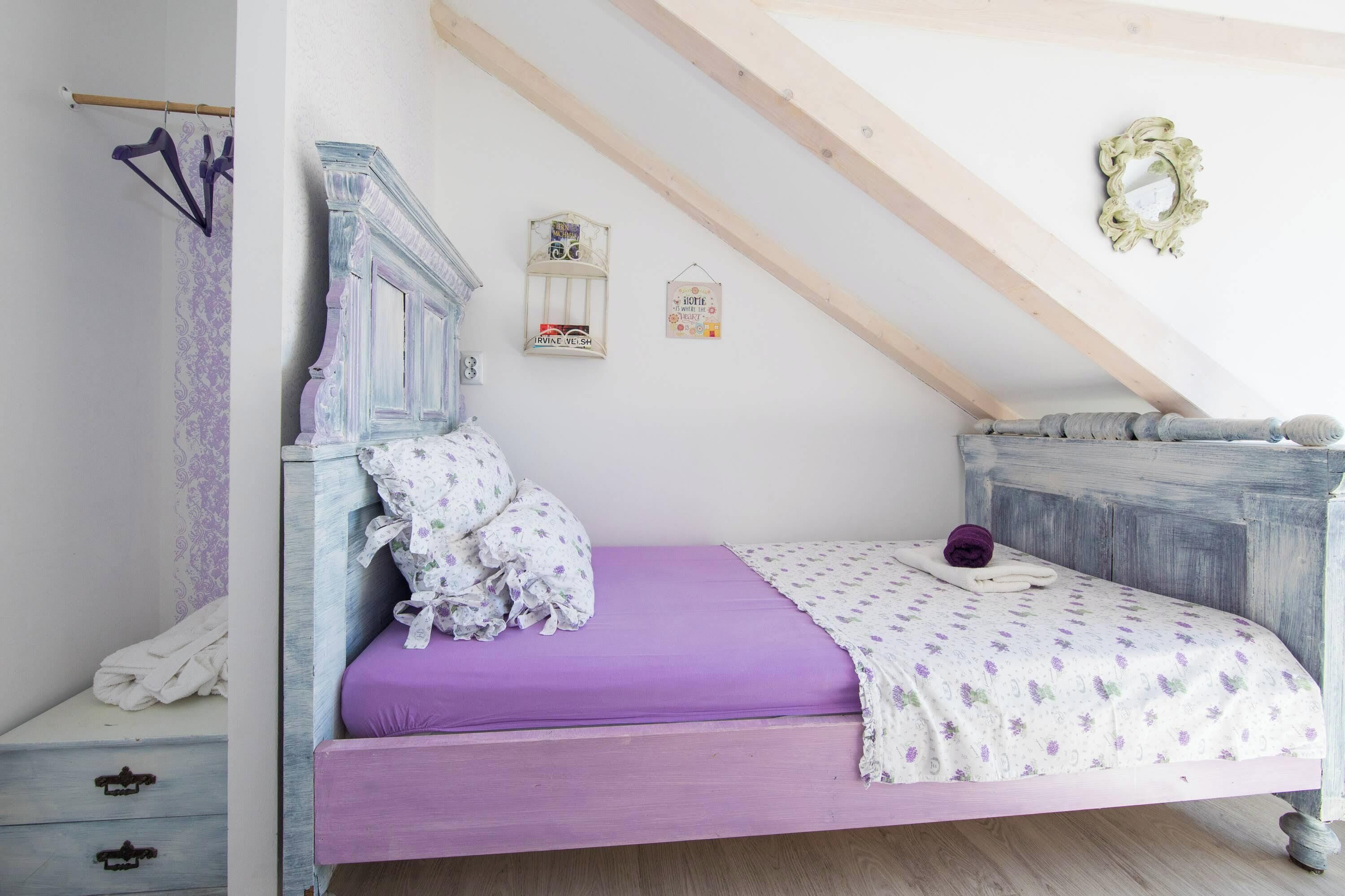 A bedroom with a purple bed, a wooden headboard, and a sloped ceiling with exposed beams.