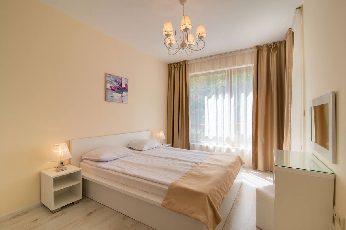 A bedroom with a bed, bedside tables, a lamp, a mirror, and a window with curtains.