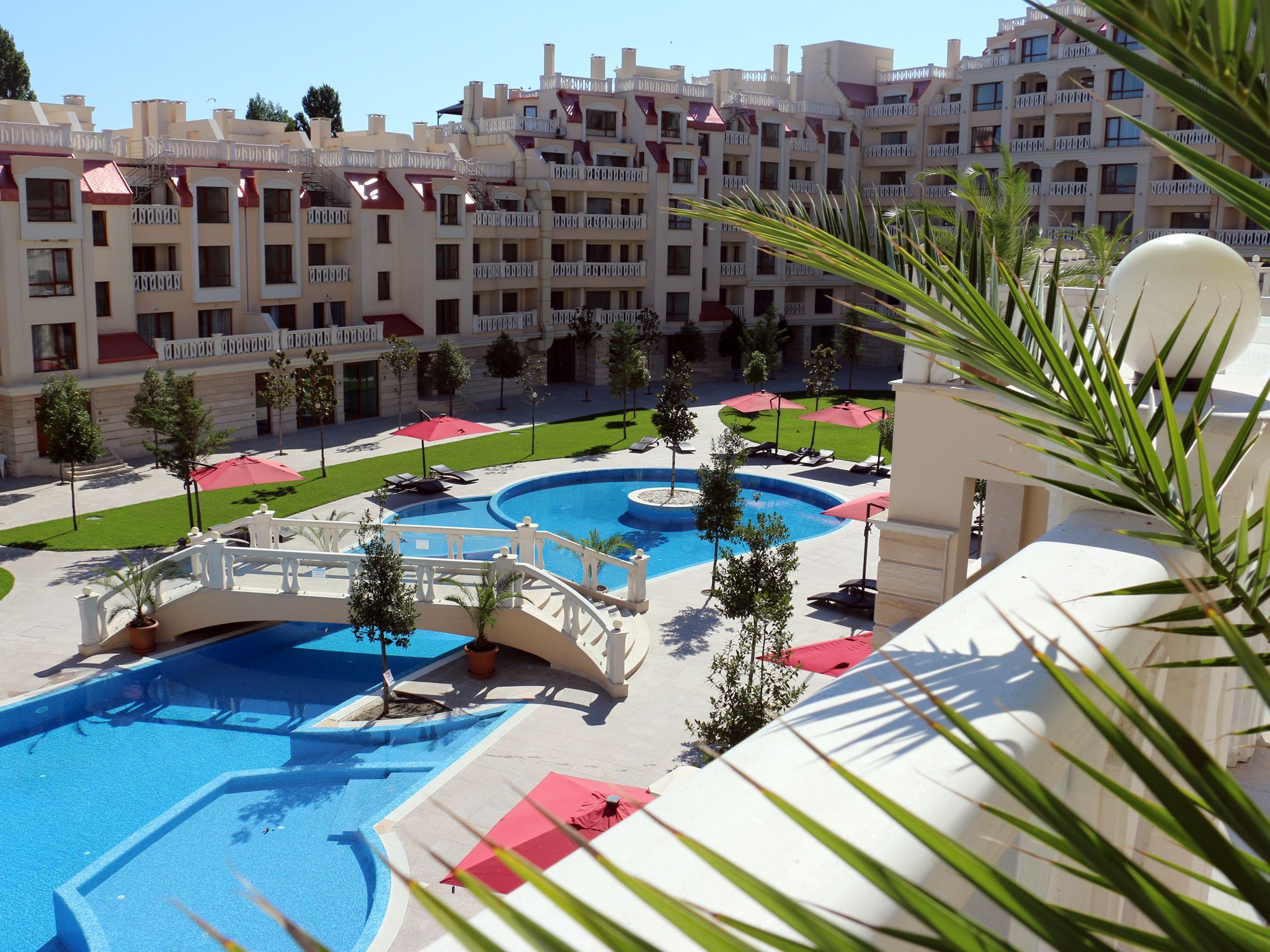 Un hotel con varios balcones, piscina y un césped bien cuidado.
