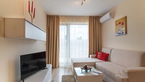 A modern living room with a flat-screen TV, a beige sofa, a coffee table, and a painting on the wall. - Varna South Bay Apart Complex (Varna)