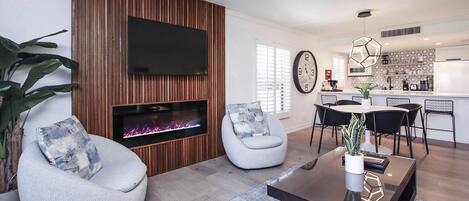 A modern living room with a fireplace, two accent chairs, a coffee table, and a kitchen area with a dining set.