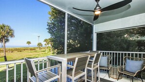 Veranda coperta all'aperto con tavolo e sedie, una ventola a soffitto e vista sull'oceano e sugli alberi.