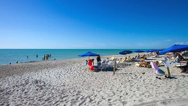 Una spiaggia con persone, ombrelloni e lettini.
