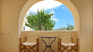 A balcony with two wooden chairs and a small table, framed by a large archway. - Dagris Villa Studios (Santorini)