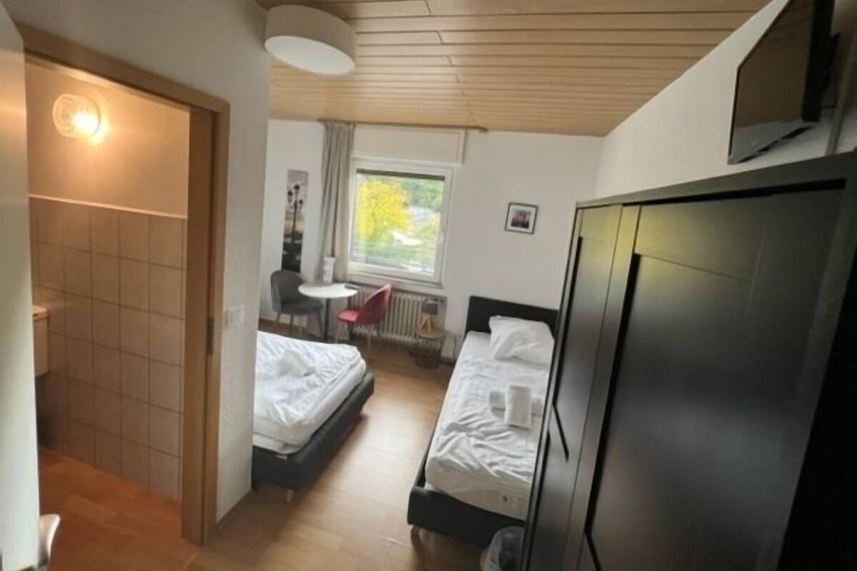 Pieni hotellihuone, jossa on kaksi sänkyä, pieni pöytä, tuoli, patteri ja seinälle asennettu televisio.