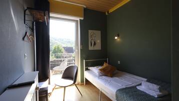 Una habitación pequeña con una cama individual, un escritorio de madera, una silla y una ventana con vistas a un balcón.