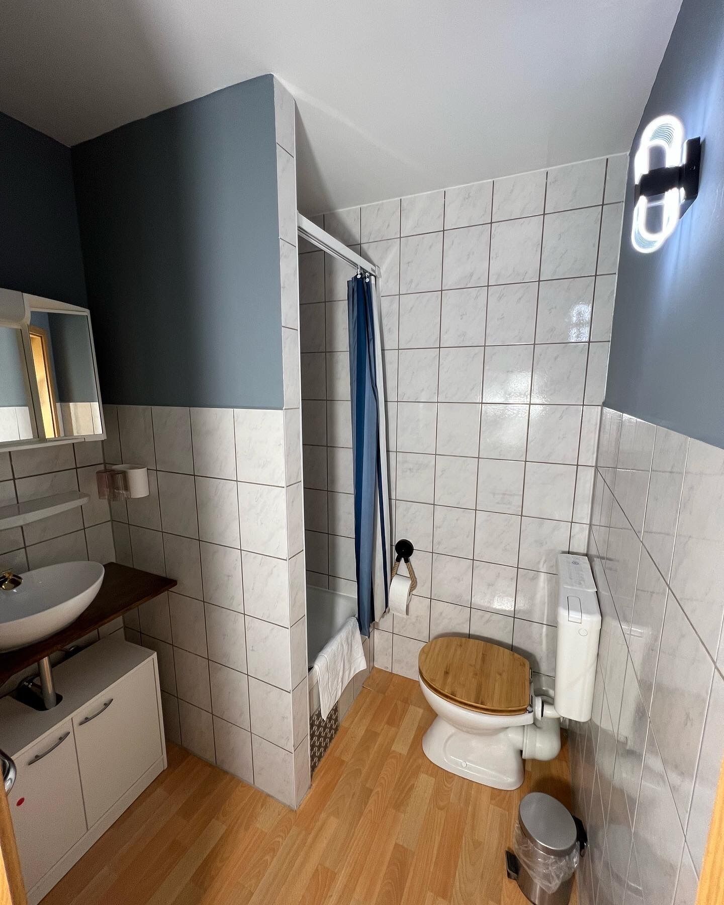 Un baño pequeño con un lavamanos blanco, inodoro de madera y cortina de ducha.