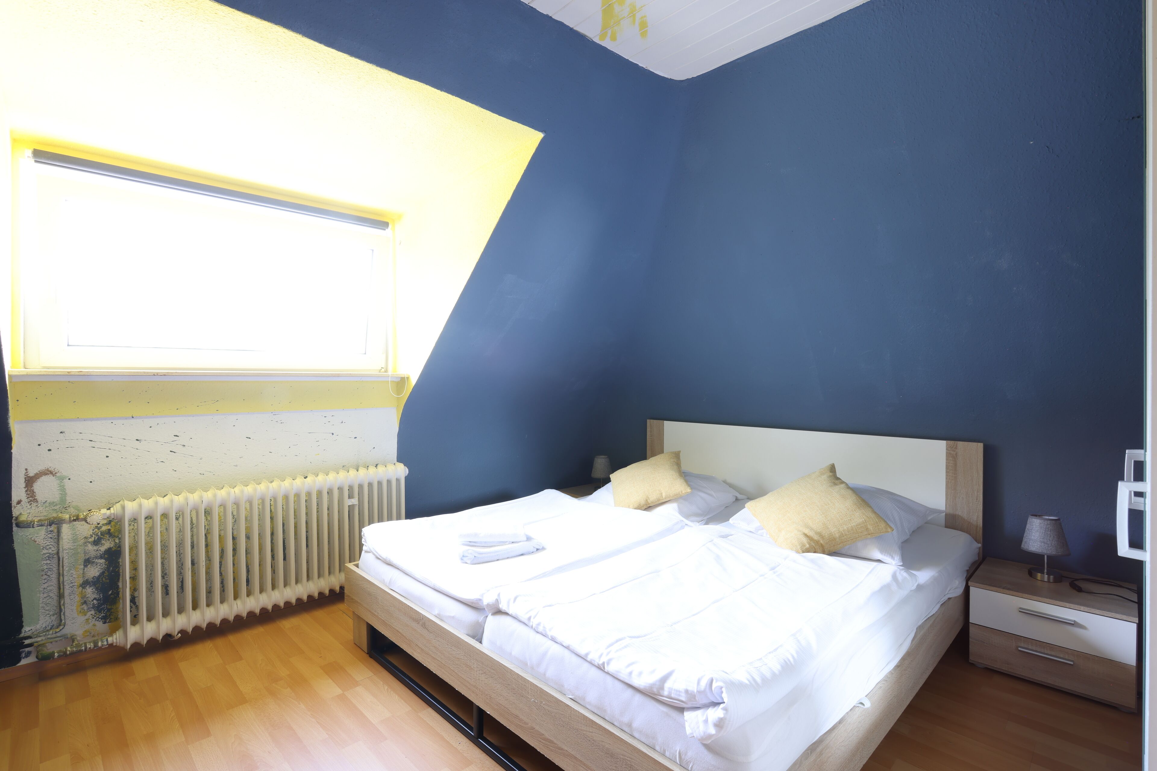 A bedroom with a bed, bedside table, lamp, and a window with a view of the outside.
