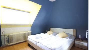 A bedroom with a bed, bedside table, lamp, and a window with a view of the outside.