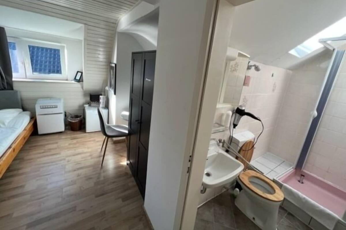 Pieni huone, jossa on sänky, pieni työpöytä, tuoli, wc ja suihku.