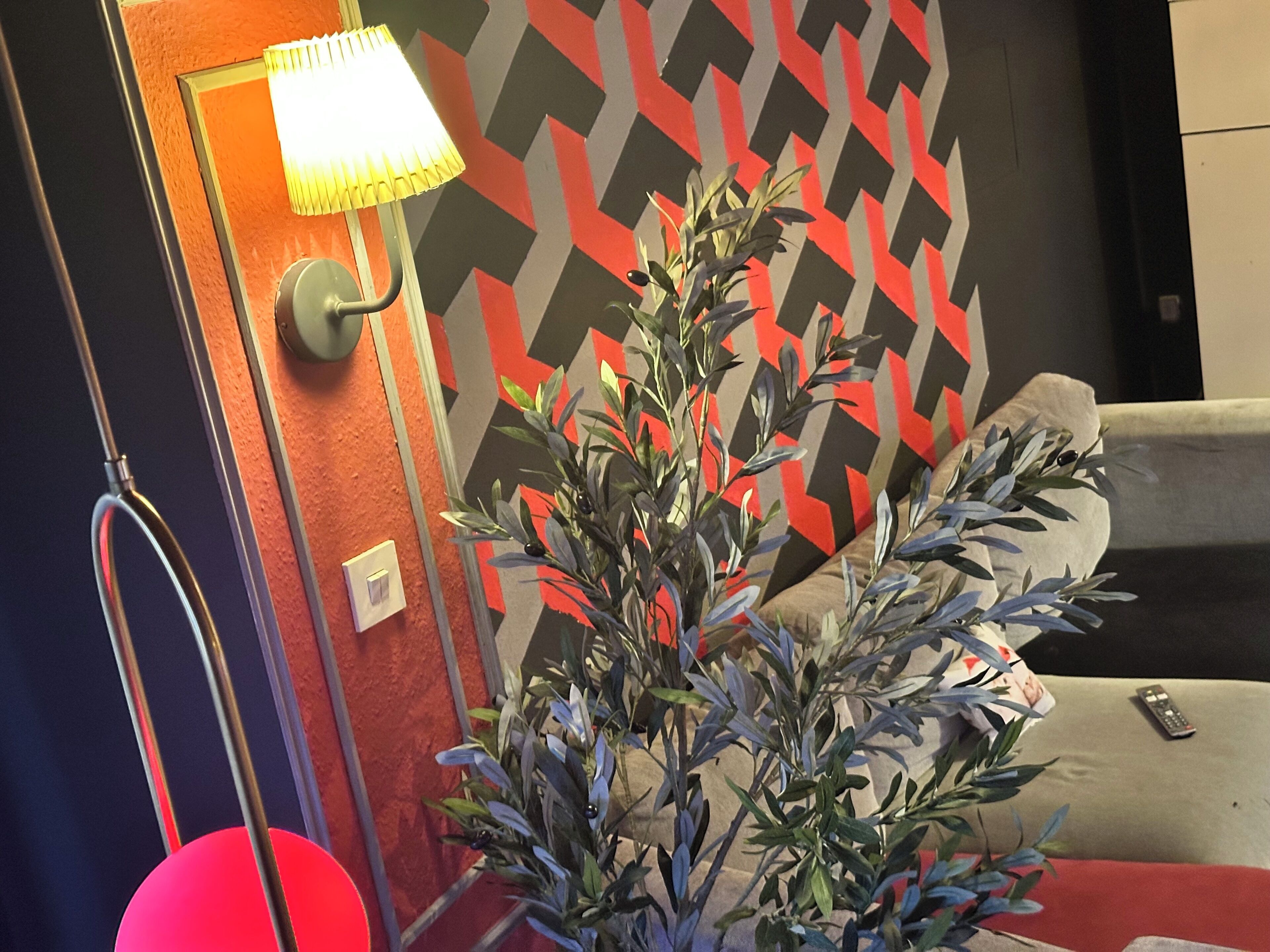 A room with a modern lamp, a potted plant, and a patterned wall.