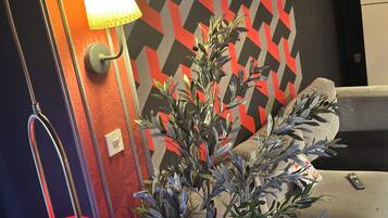 A room with a modern lamp, a potted plant, and a patterned wall.