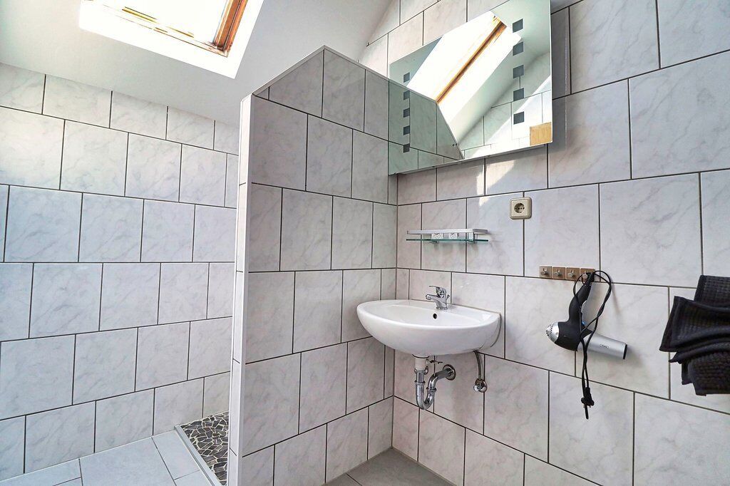 A modern bathroom with a skylight, a white sink, and a hairdryer on the wall.