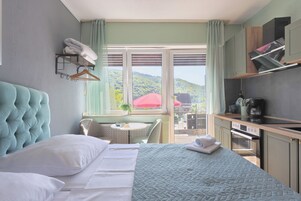Habitación de hotel con cama, una mesita, una silla, ventana con vista a follaje y una kitchenette.