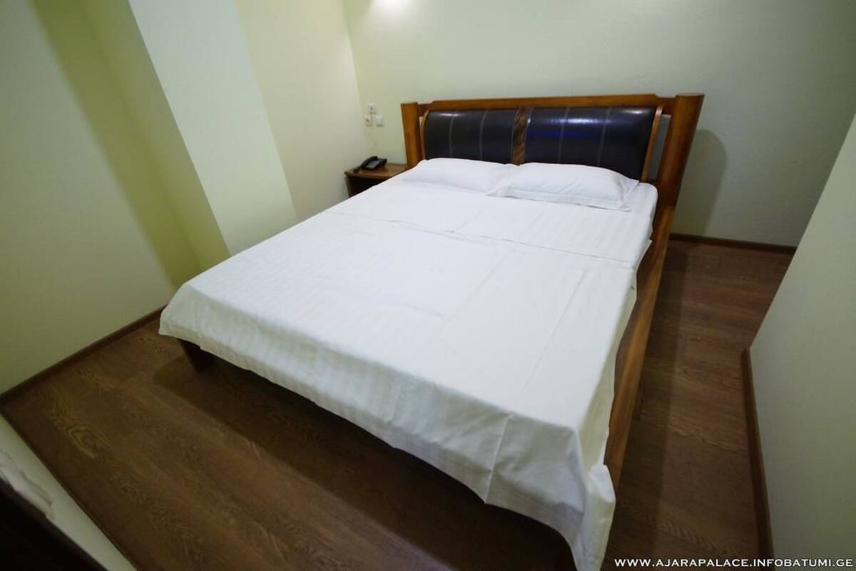 A neatly made bed in a room with a wooden floor and a simple nightstand with a phone.