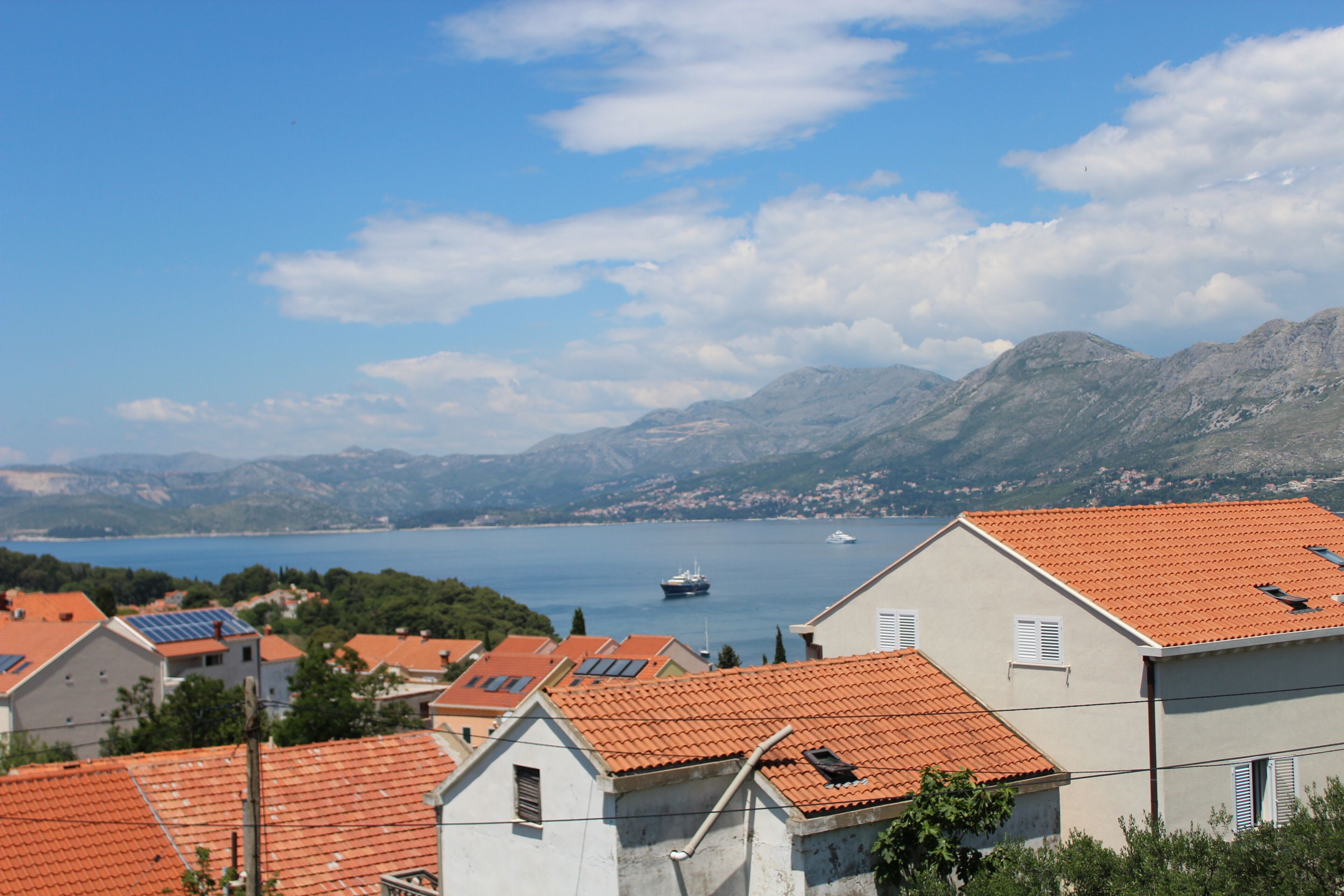 A coastal town with red-tiled roofs, a body of water, and mountains in the background.