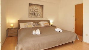 Uma cama bem arrumada com um cobertor marrom, duas toalhas enroladas e uma obra de arte floral acima.