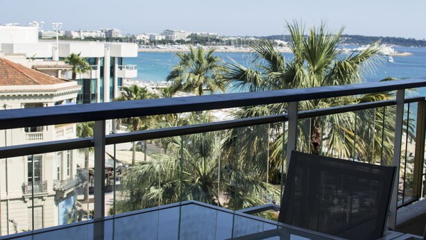Een balkon met uitzicht op zee, palmbomen en gebouwen.