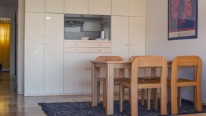 Een kleine keuken met witte kastjes, een houten eettafel en twee stoelen.