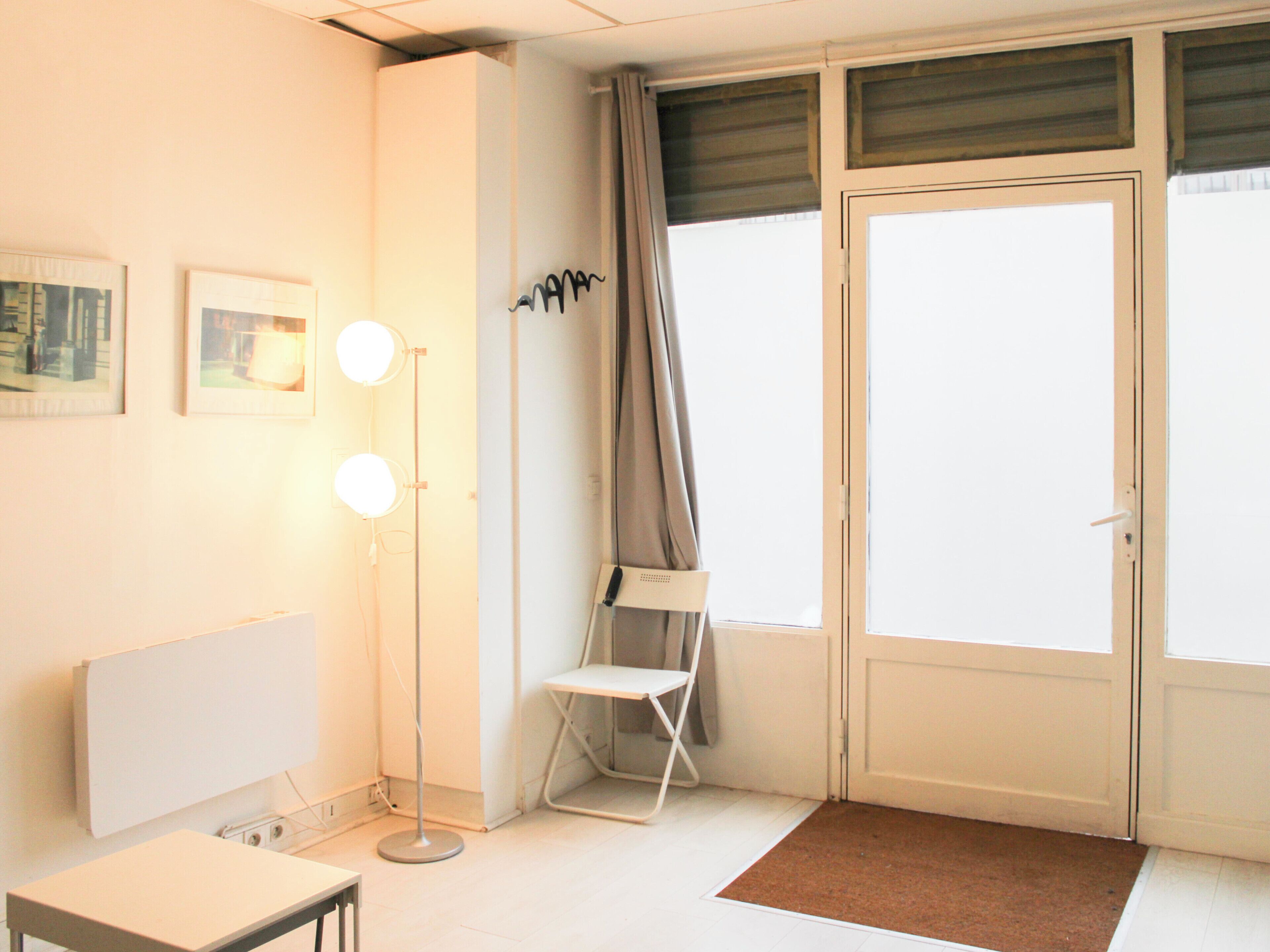 A room with a white radiator, a floor lamp, a chair, and a door with curtains.