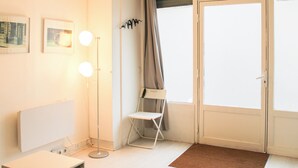 A room with a white radiator, a floor lamp, a chair, and a door with curtains. - Souplex - 4P - Batignolles (Paris)