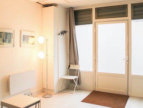 A room with a white radiator, a floor lamp, a chair, and a door with curtains.