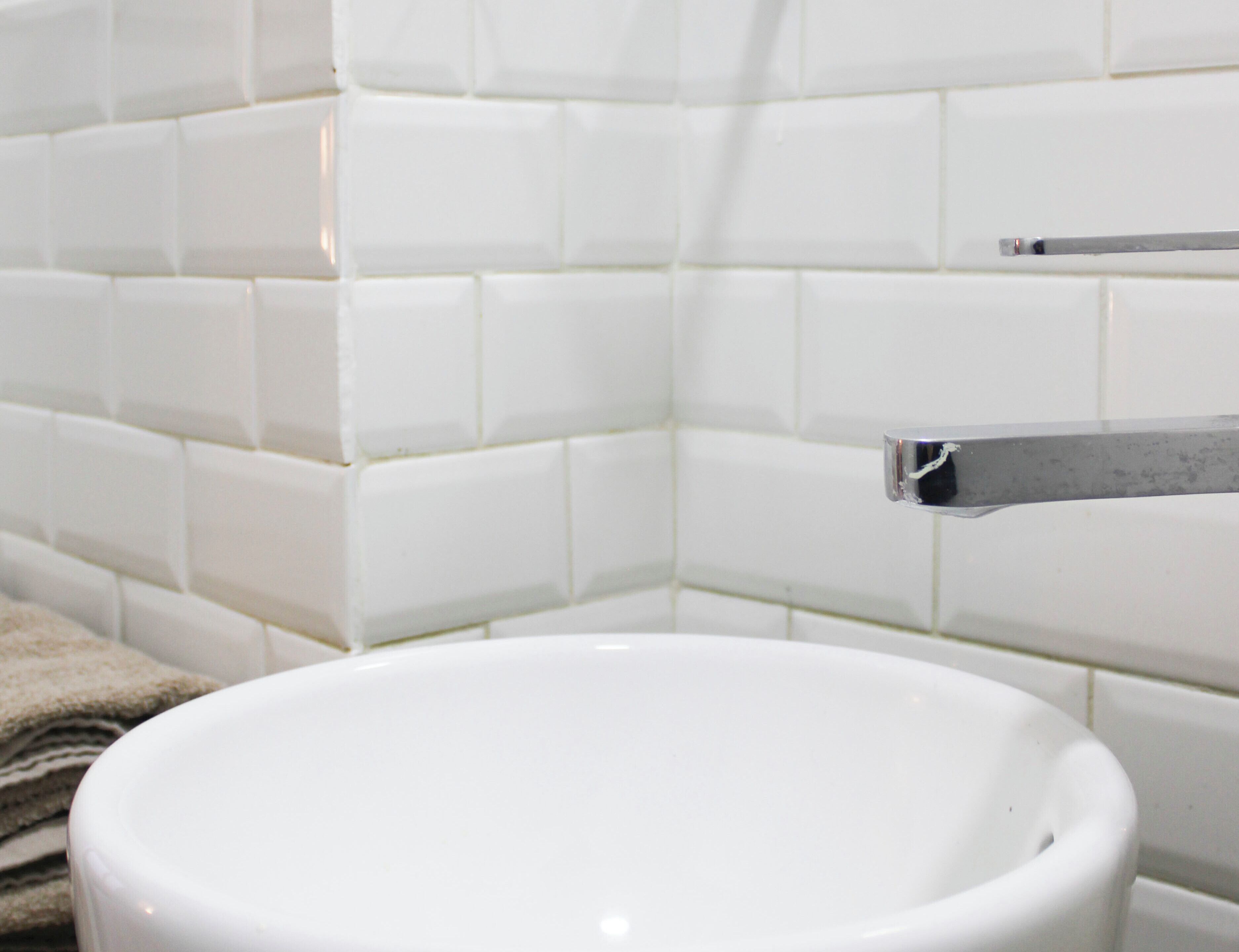 A bathroom with white tiled walls and a white sink.