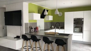 A modern kitchen with a central island, bar stools, a built-in oven, and a clock on the wall. - House villas with swimming pool on Nîmes (Nîmes)