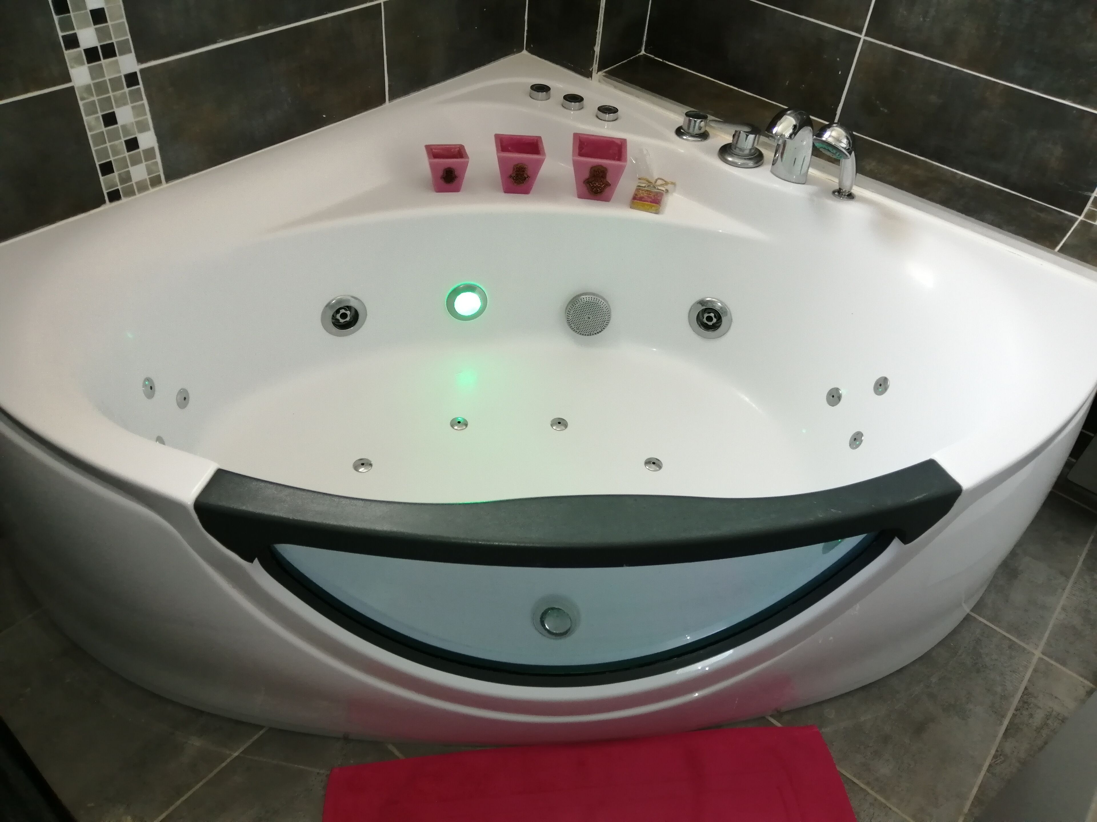 Une grande baignoire blanche avec un bord noir, plusieurs robinets et un éclairage vert.