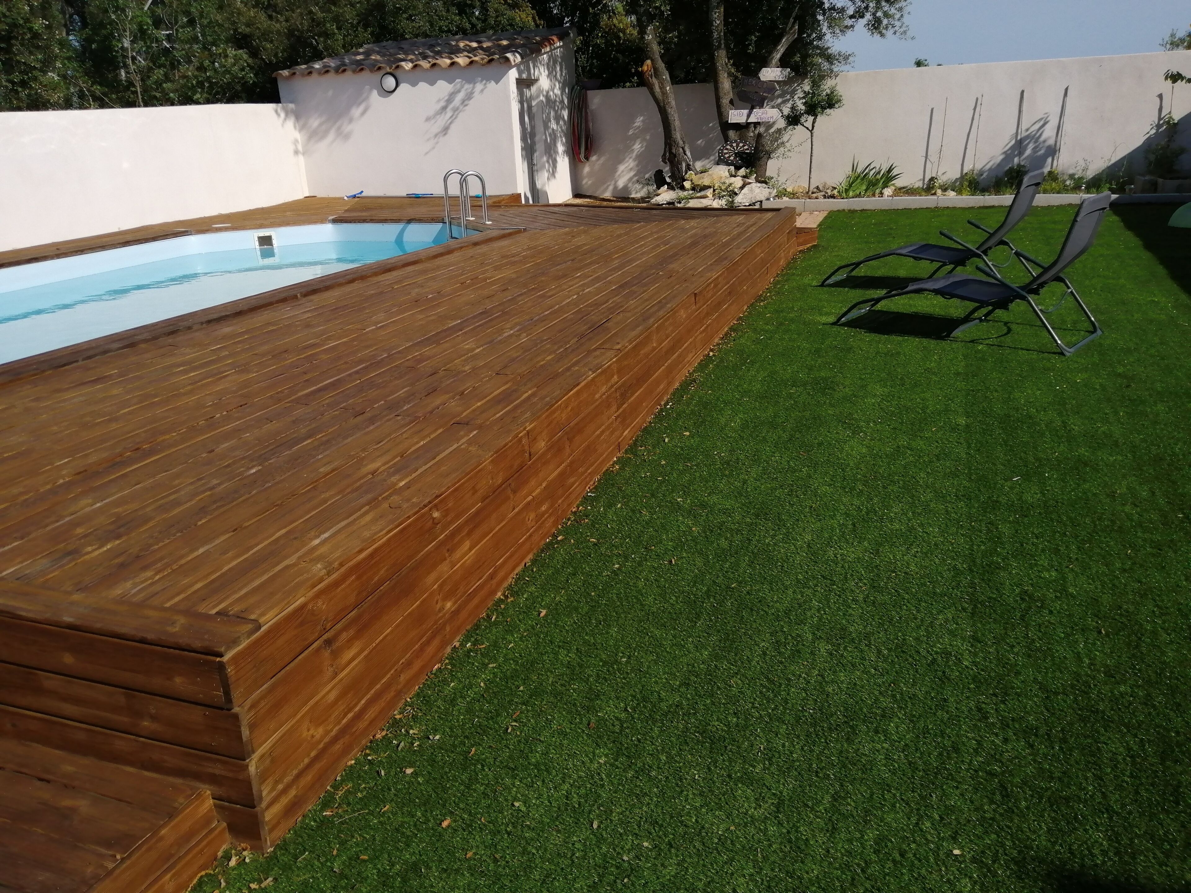 Una piscina con plataforma de madera y césped artificial.