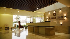 A reception area with a wooden reception desk, a large window with a view of palm trees, and a modern ceiling design. - Ashok Inn (Davanagere)