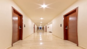 A long, well-lit hallway with wooden doors on both sides, leading to a bright room at the end. - Ashok Inn (Davanagere)