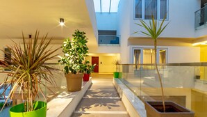 A modern indoor corridor with potted plants, a skylight, and a glass railing. - Ashok Inn (Davanagere)