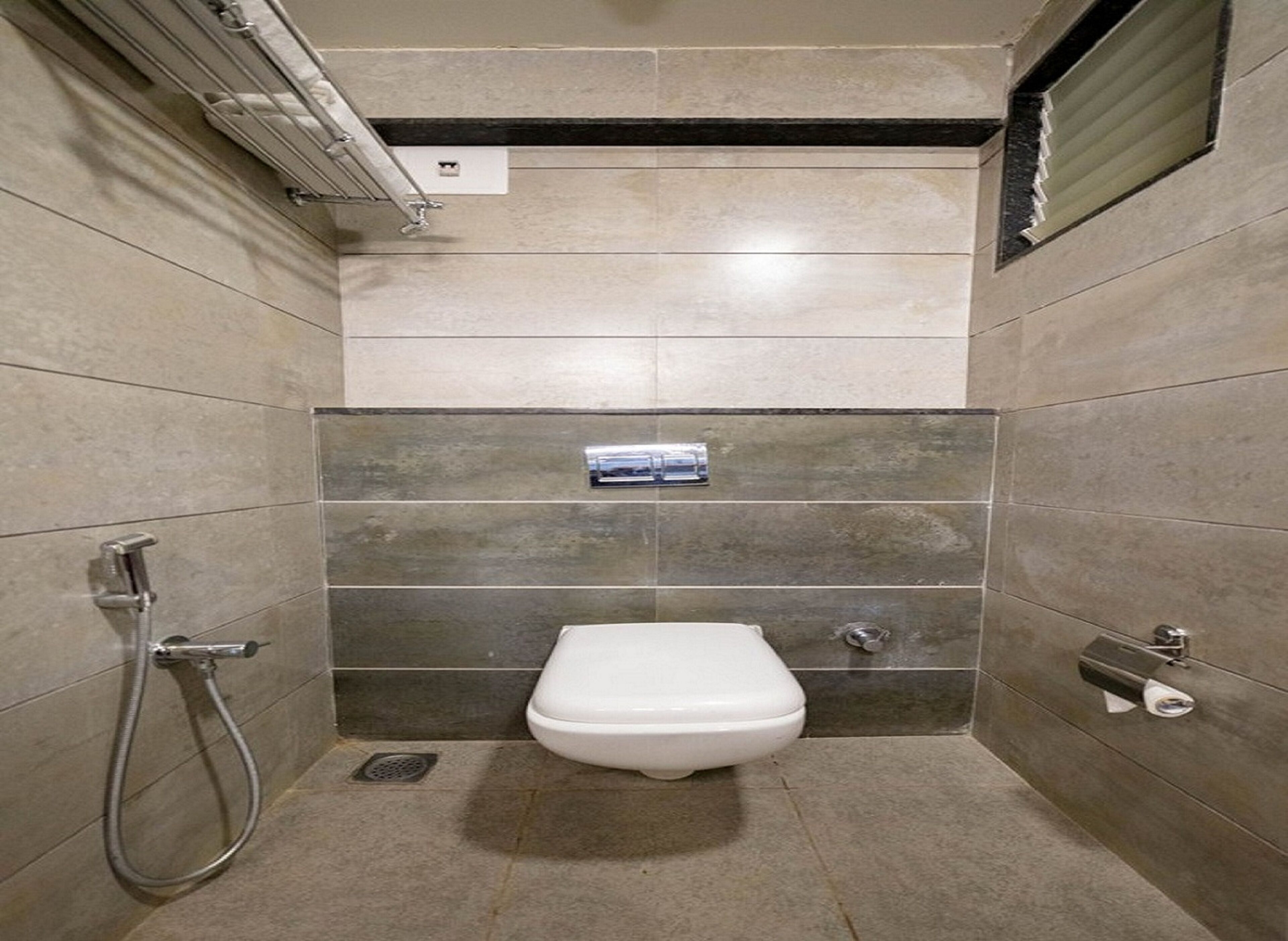 A small, tiled bathroom with a toilet, a shower, and a towel dispenser.