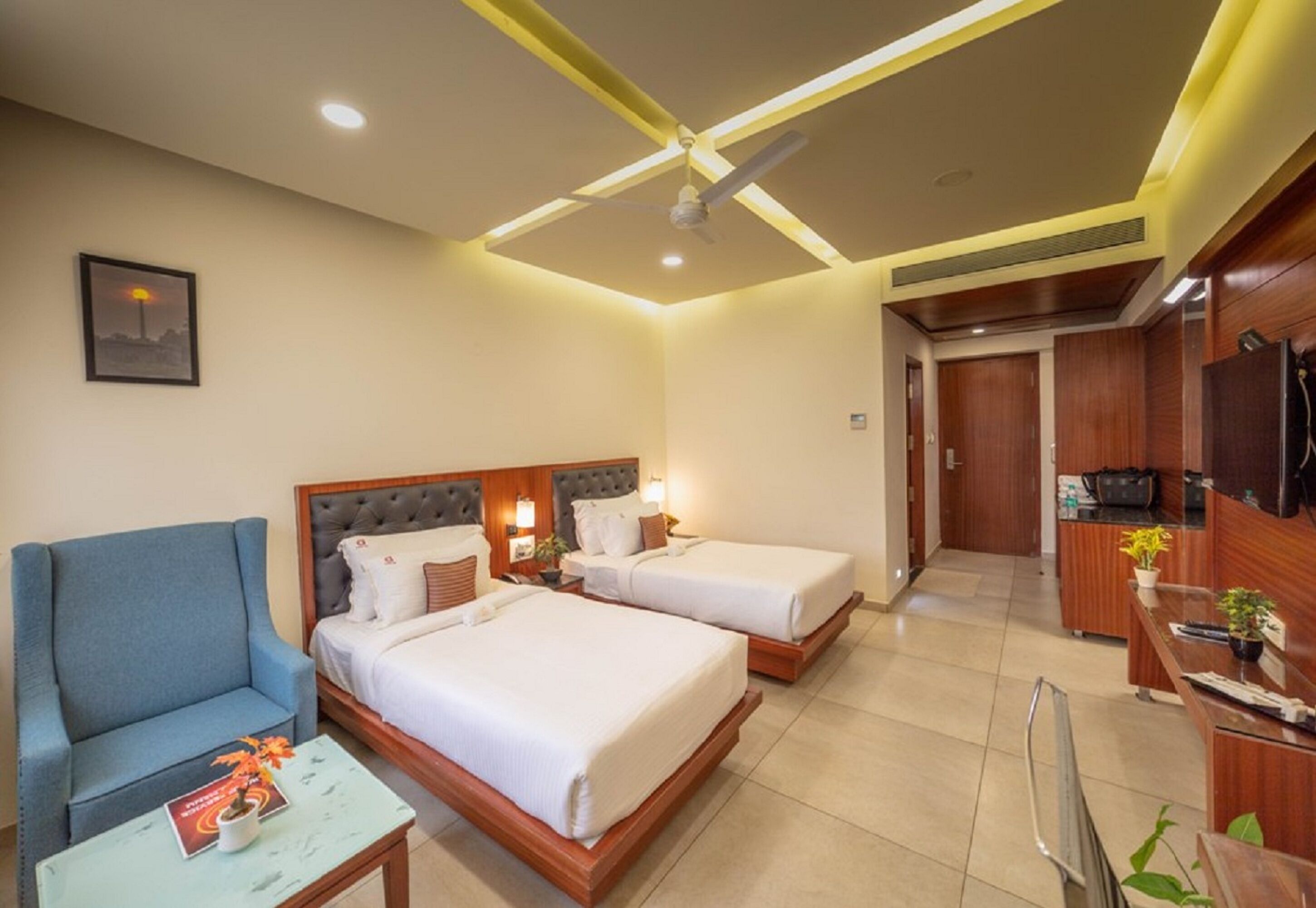 A hotel room with two beds, a sofa, a small table, a TV, and a kitchenette.