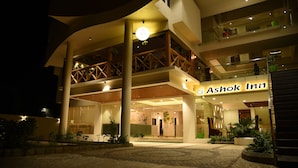 A multi-story hotel with a prominent entrance, outdoor seating area, and a well-lit atrium. - Ashok Inn (Davanagere)