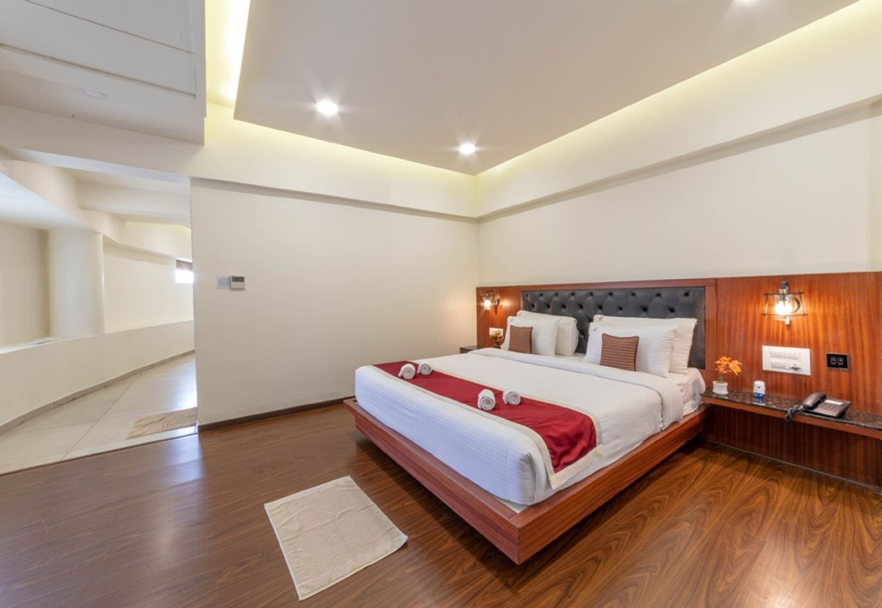 A modern hotel room with a large bed, wooden flooring, and a built-in headboard.