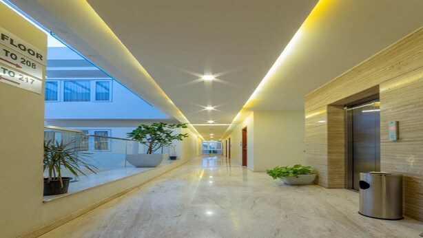 A modern hotel corridor with a marble floor, directional signs, potted plants, and an elevator. - Ashok Inn (Davanagere)