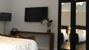 Ein Hotelzimmer mit einem Bett, einem flachbildfernseher an der Wand, einem Holztisch, einem Spiegel und einer Tür zu einem anderen Raum.