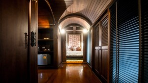 A hallway with wooden flooring, a bed with a floral bedspread, and a closed sliding door on the right.