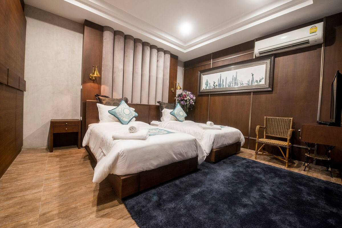 Een hotelkamer met twee bedden, een klein nachtkastje, een stoel, een bureau en een kunstwerk in een lijst aan de muur.