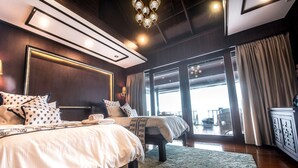 A modern hotel room with a large bed, a separate sofa, a large window, and a balcony.