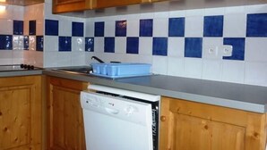 Una cocina con armarios de madera, microondas, lavavajillas y baldosas blancas y azules a cuadros.