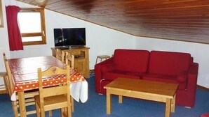 Una habitación acogedora con techo de madera, un sofá rojo, una mesa de madera y un televisor sobre un mueble de madera.