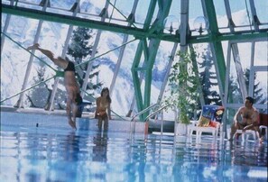 Une piscine dotée d’un toit en verre, entourée d’arbres et de quelques personnes.