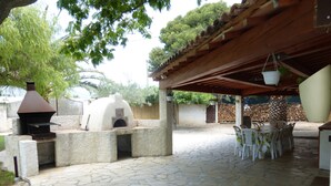 Un patio al aire libre con suelo de piedra, un horno de ladrillo y una zona de estar cubierta con sillas de plástico.