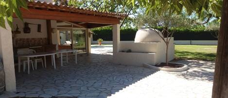 A patio with stone flooring, a wooden pergola, a dining table with chairs, and a small tree.