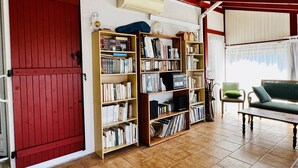 Una habitación con puerta roja, una estantería, una silla verde y una mesa.