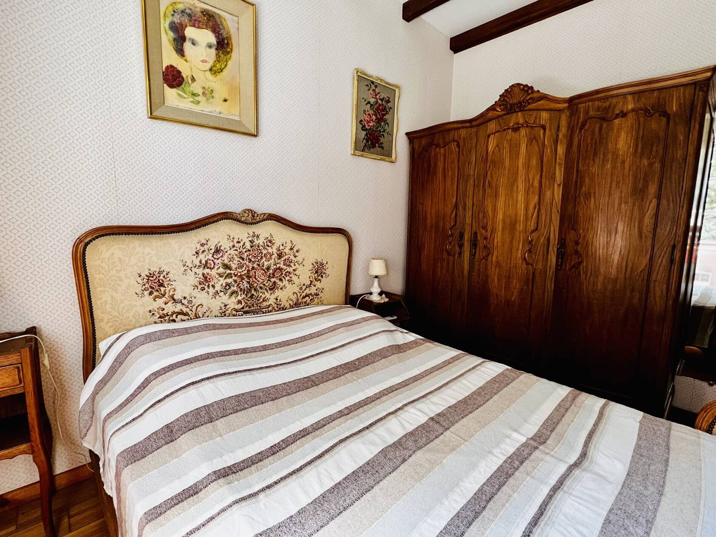 Een slaapkamer met een bed, een houten garderobe en twee ingelijste foto’s aan de muur.
