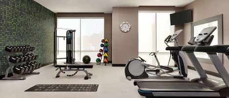 Une salle de sport équipée de tapis de course, d’haltères, d’un support à squats et d’un téléviseur fixé au mur.